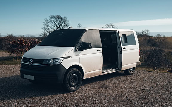 White Volkswagen campervan parked outdoors with windscreen cover, ideal for protecting your vehicle during spring. Perfect for campervan and motorhome owners seeking warmth, privacy, and protection.