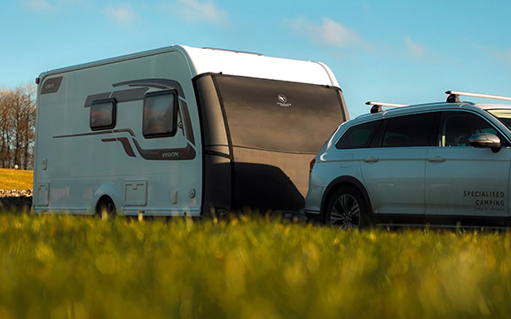A caravan hitched to a car on a scenic spring day, highlighting towing safety and preparation for caravan trips.
