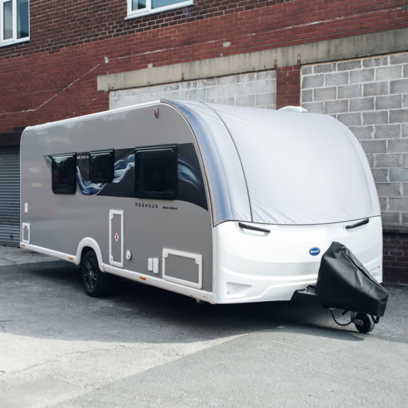 Modern caravan with panoramic window cover parked against a brick wall, featuring sleek design and black window accents.