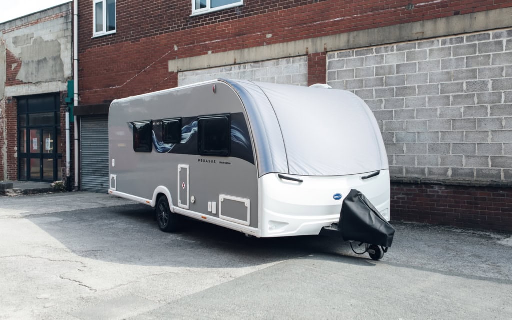 Contemporary caravan featuring large panoramic windows and sleek design, parked on an urban street with brick and concrete buildings in the background.