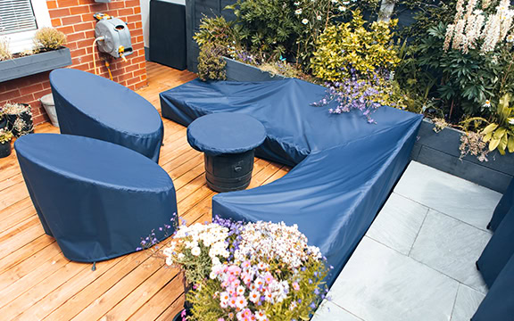 Durable blue garden furniture covers protecting outdoor seating on a wooden patio with lush greenery and flowers.