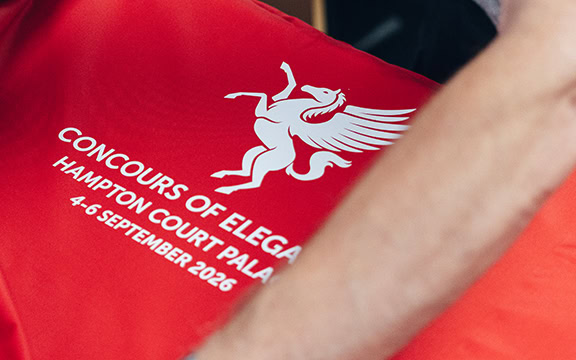 Red car cover with Concours of Elegance logo and event details for 2026 at Hampton Court Palace.
