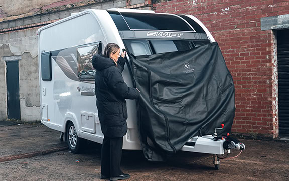 Woman fitting a custom-made towing cover on a caravan in an urban setting, showcasing specialised vehicle cover solutions.