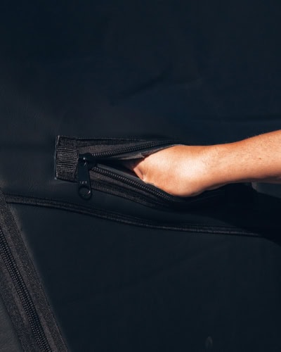 Bright, close-up shot of a person’s hand reaching into a zippered pocket on a black vehicle cover, showcasing the rugged waterproof material, durable zipper, and secure fit designed for tow pro elite transport protection.