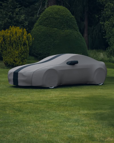 An Aston Martin with a custom indoor cover on it in grey with a black stripe and piping.
