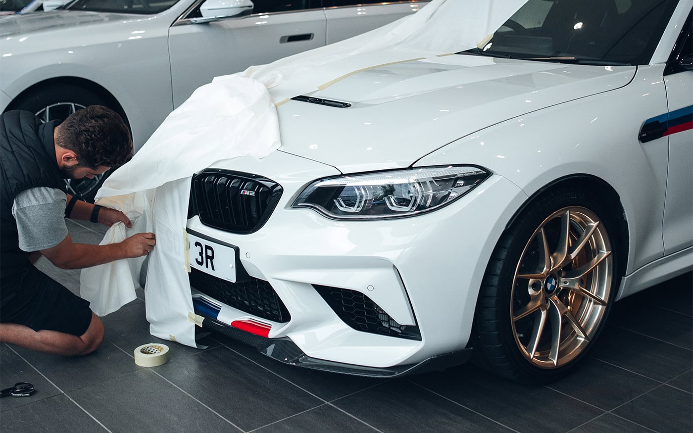 A close up of a BMW M2 with a designer tailoring a pattern for a car cover.