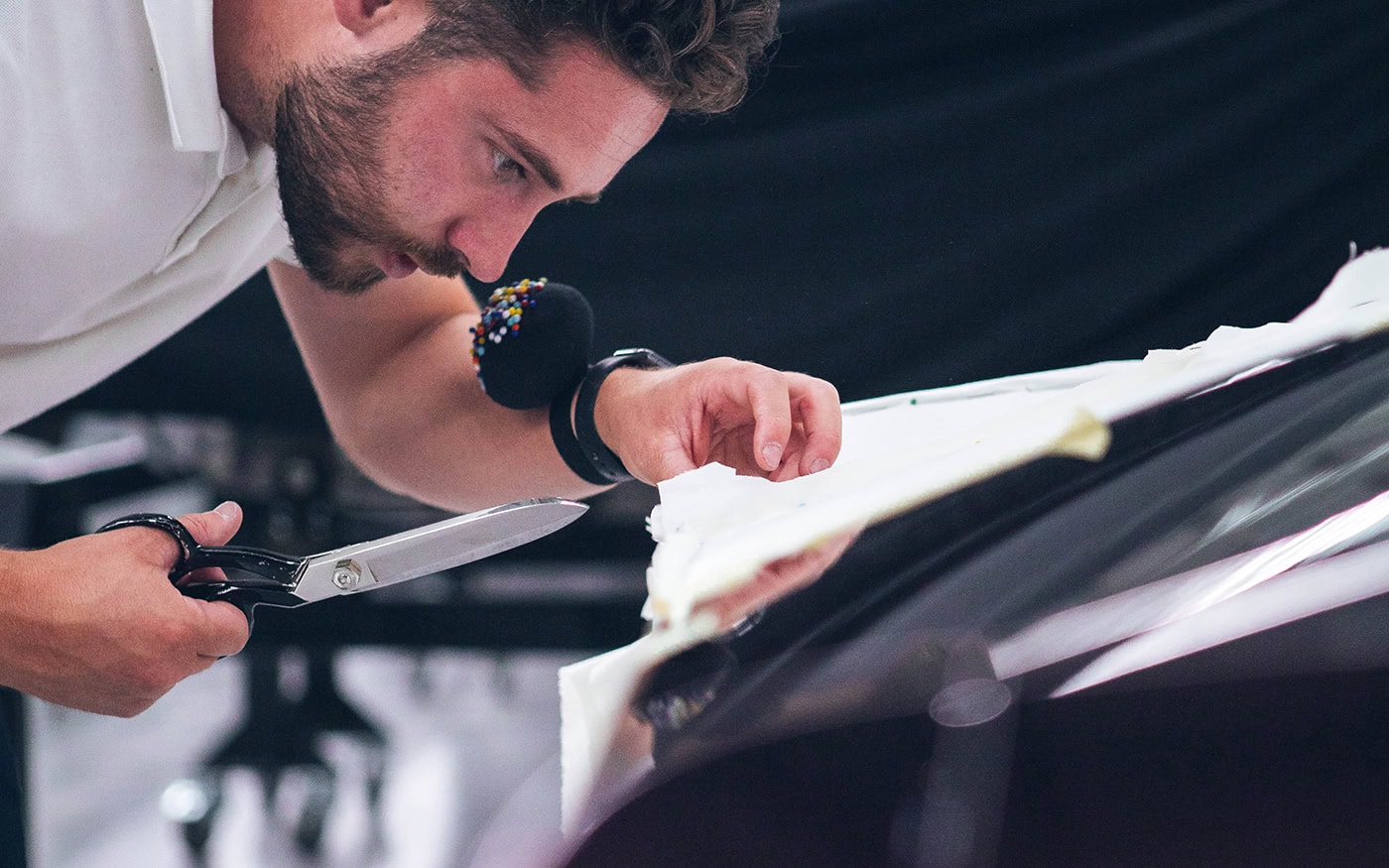 A picture of a designer cutting cloth with scissors to tailor a pattern for a car cover.