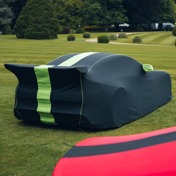 A black Aston Martin Indoor car cover with green stripes, piping and wing mirrors.