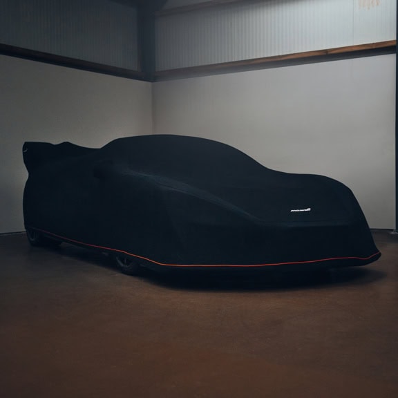 A Mclaren Senna with an indoor cover on finished in black with an orange piping line.