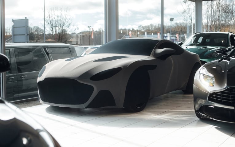 High-quality car cover protecting a luxury sports car in a showroom setting, with multiple vehicles around, showcasing premium vehicle protection solutions.