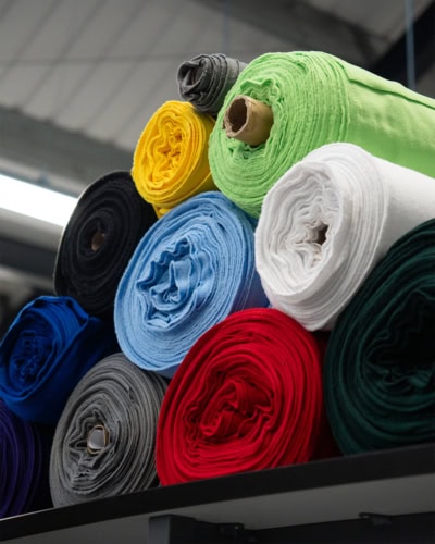 Brightly coloured rolls of fabric stored indoors for covers, upholstery, and protective solutions. Customisable fabric covers for furniture and equipment, delivered by Specialised Covers.