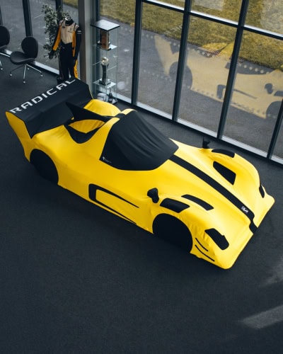 1. Custom yellow racing car cover protecting race cars at Specialised Covers showroom with black accents and aerodynamic design.