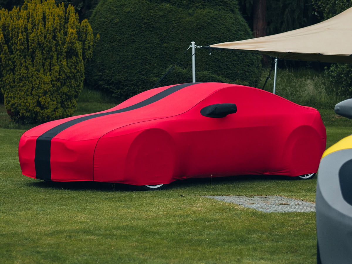 Durable outdoor car cover in vibrant red with black racing stripe, waterproof and UV resistant, ideal for safeguarding vehicles. Custom fit for a sleek, sporty appearance.