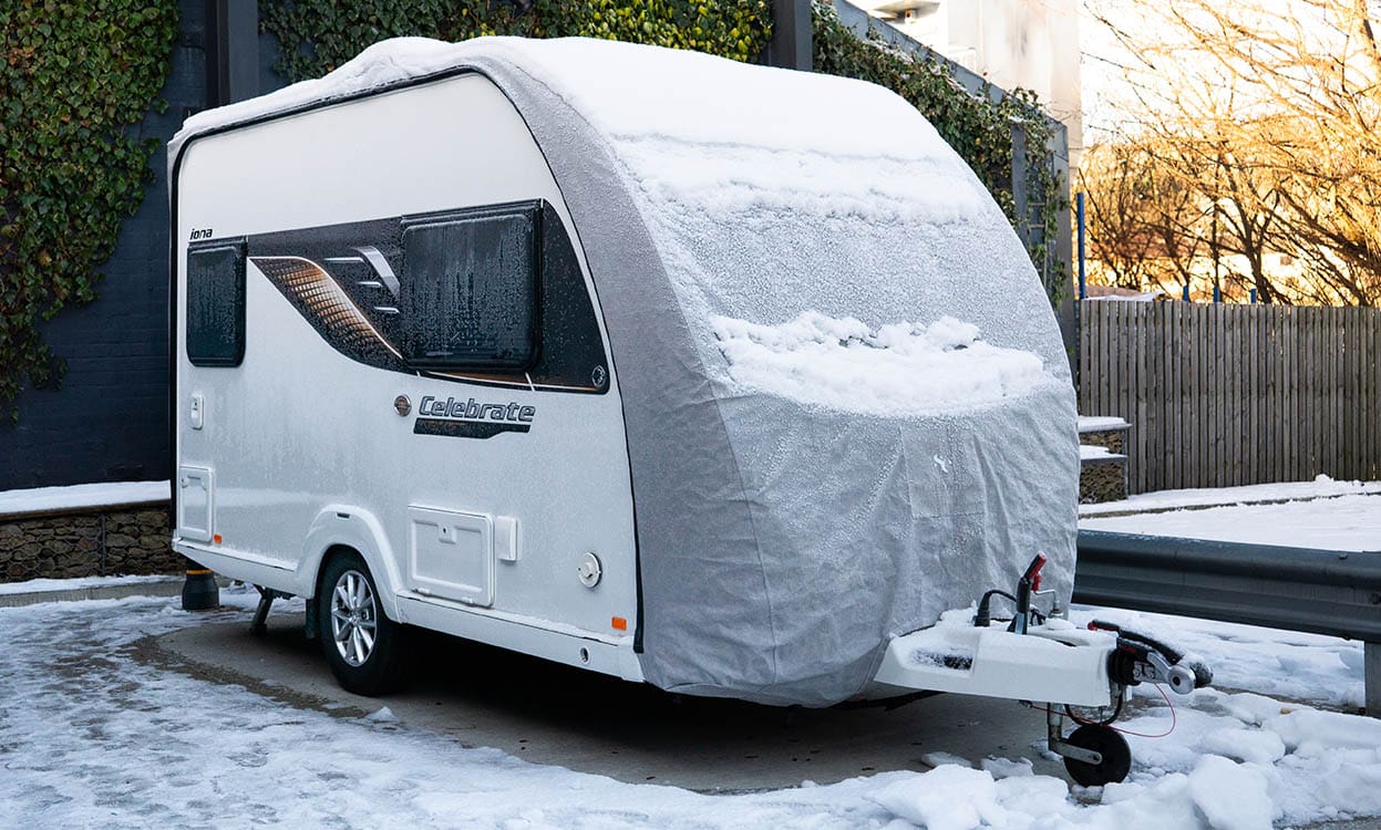 Snow-covered caravan with weatherproof cover in snowy environment, outdoor caravan protection, durable outdoor cover, weatherproof caravan cover for winter.
