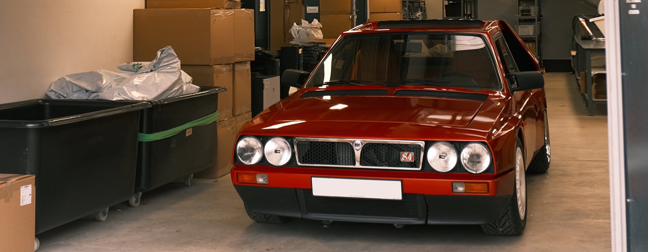 1. Classic red Lancia Delta Integrale car with protective cover in an indoor storage facility, showcasing the vintage vehicle's iconic design and condition.