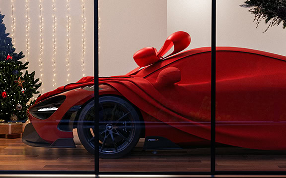 Aston Martin supercar wrapped in festive red cover with large bow, displayed behind a glass window.