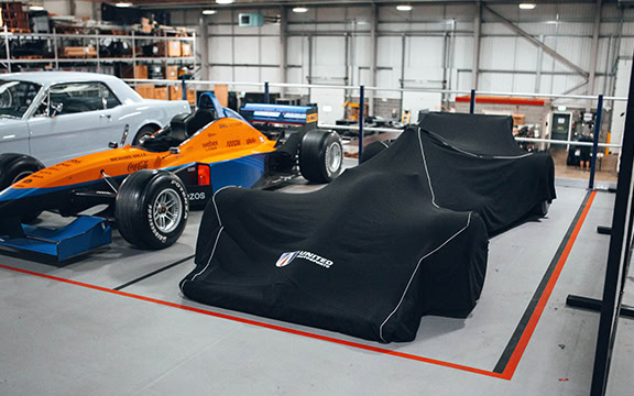 High-quality custom car covers protecting classic and race cars, including Formula 1 vehicles, made by Specialised Covers for superior fit and durability in professional automotive environments.