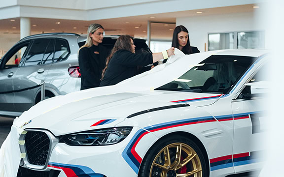 Women unveiling a custom vehicle wrap at Specialised Covers during International Women’s Day.