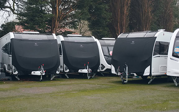 A row of caravans fitted with universal towing covers protecting them from weather and debris during transport.