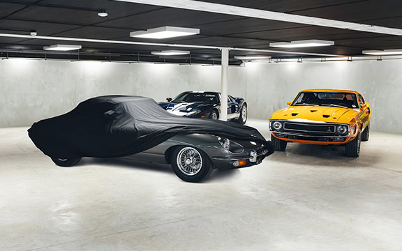 High-quality car cover protecting a classic black sports car and other vehicles in an indoor garage setting, ensuring dust and damage prevention.