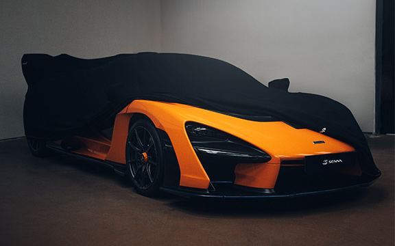 High-end orange supercar partially covered with a protective car cover in a dimly lit garage setting.