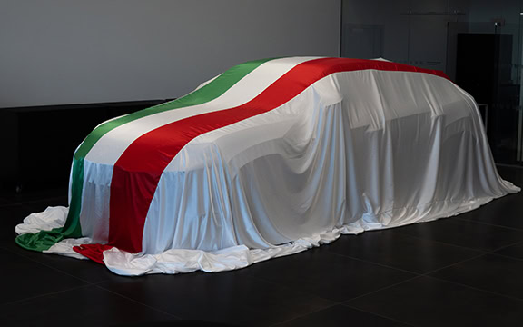 A detailed car cover with the colours of the Italian flag, draped over a vehicle indoors.