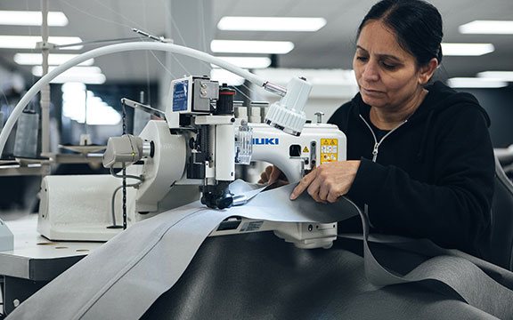 Female worker operating industrial sewing machine in textile factory, focusing on fabric production.