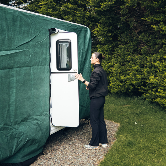 Woman opening a caravan door covered with a durable green storage cover, protecting the caravan from weather and damage.