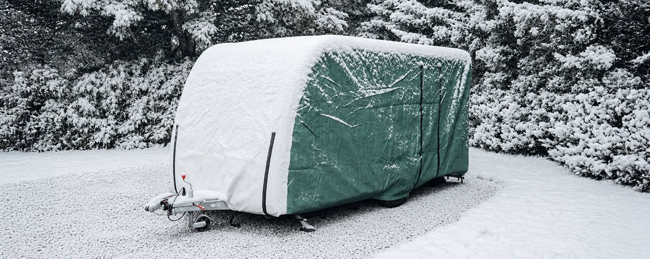 Caravan covered with a full protective cover in a snowy outdoor setting, safeguarding it from winter weather.